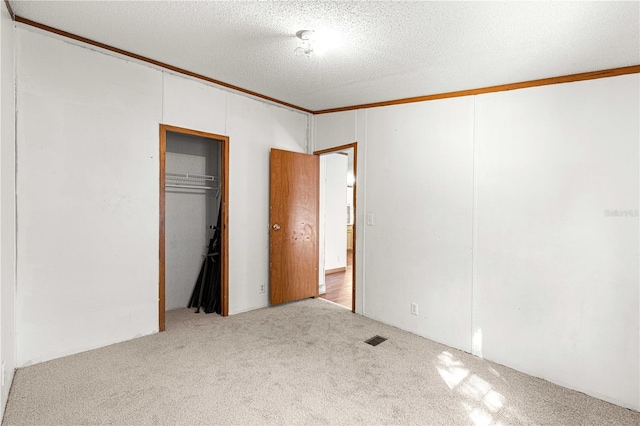 unfurnished bedroom featuring a textured ceiling, crown molding, light carpet, and a closet