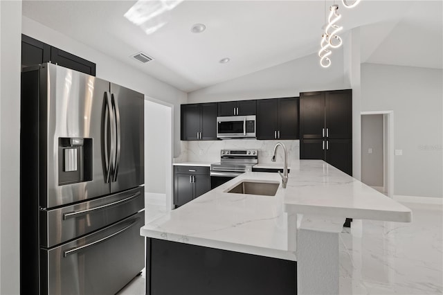 kitchen featuring decorative light fixtures, a kitchen island with sink, appliances with stainless steel finishes, and vaulted ceiling