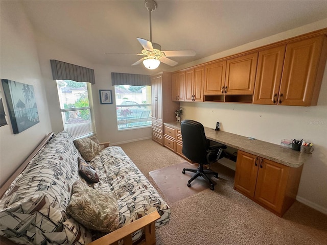 home office featuring built in desk, light colored carpet, and ceiling fan