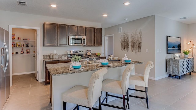 kitchen with a breakfast bar, light stone countertops, an island with sink, and stainless steel appliances