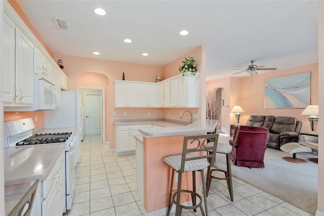 kitchen featuring white appliances, white cabinets, ceiling fan, a kitchen bar, and kitchen peninsula