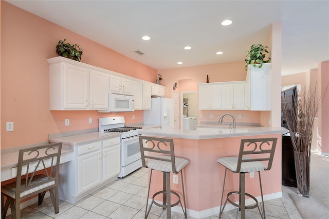 kitchen with light tile patterned floors, white appliances, white cabinetry, and a kitchen breakfast bar