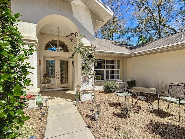 entrance to property featuring french doors, roof with shingles, and stucco siding