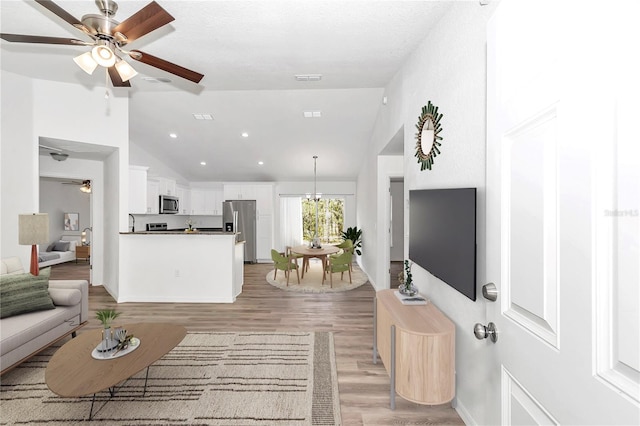 living room with ceiling fan with notable chandelier, high vaulted ceiling, and light hardwood / wood-style flooring