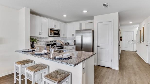 kitchen with kitchen peninsula, dark stone countertops, appliances with stainless steel finishes, white cabinets, and light wood-type flooring