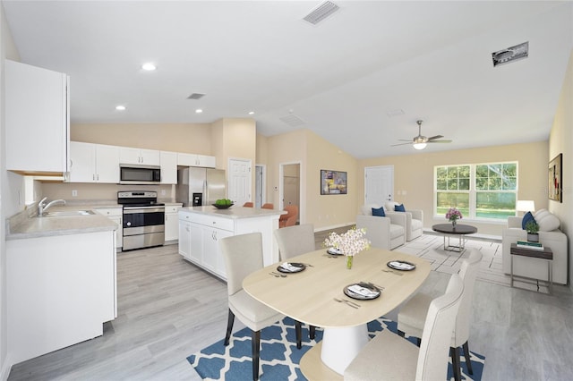 dining area with ceiling fan, sink, light hardwood / wood-style flooring, and vaulted ceiling