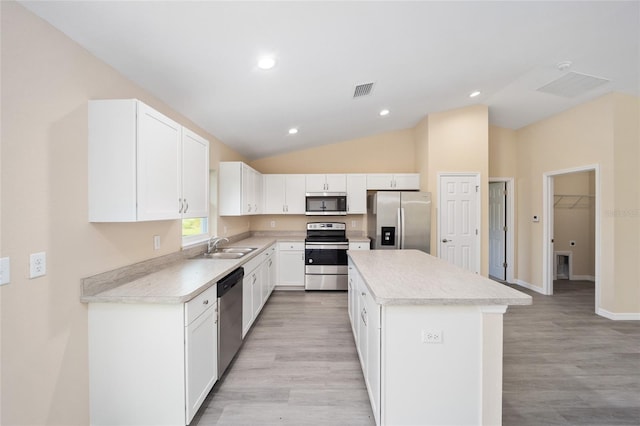 kitchen featuring appliances with stainless steel finishes, vaulted ceiling, light hardwood / wood-style flooring, a center island, and white cabinetry