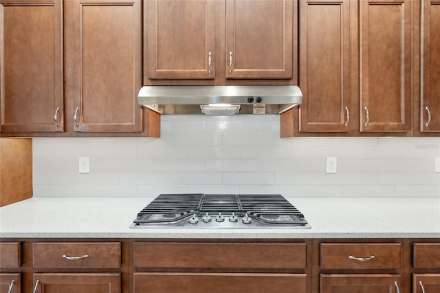 kitchen featuring backsplash, light stone counters, wall chimney range hood, and stainless steel gas cooktop