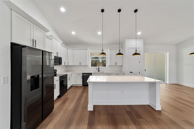 kitchen with sink, hanging light fixtures, vaulted ceiling, white cabinets, and black appliances