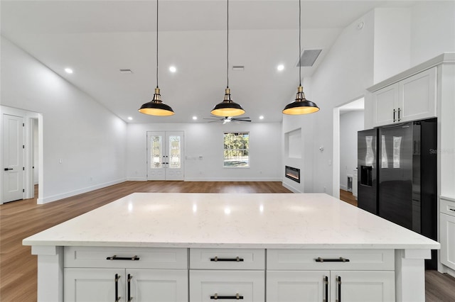 kitchen with decorative light fixtures, light stone counters, and black refrigerator with ice dispenser