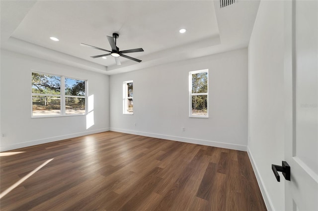 spare room with dark hardwood / wood-style floors, ceiling fan, a raised ceiling, and a wealth of natural light