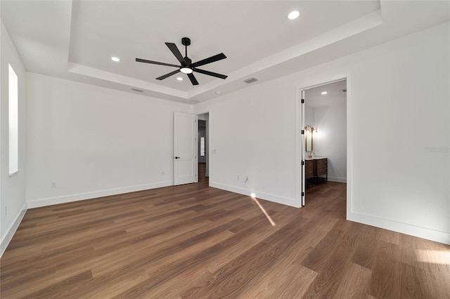 empty room featuring a raised ceiling, ceiling fan, and dark hardwood / wood-style flooring