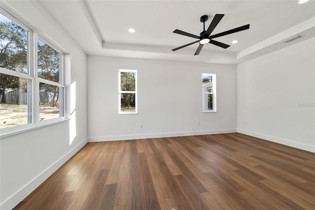 empty room with hardwood / wood-style floors, ceiling fan, and a raised ceiling