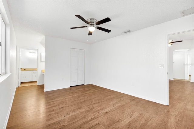 unfurnished bedroom featuring hardwood / wood-style floors, connected bathroom, a textured ceiling, and ceiling fan