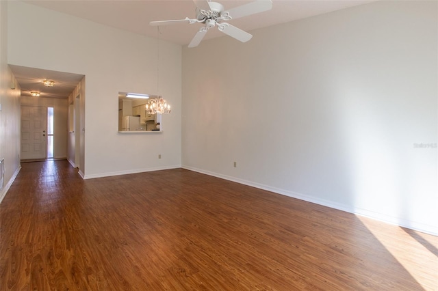 empty room with dark hardwood / wood-style floors, ceiling fan with notable chandelier, and a high ceiling