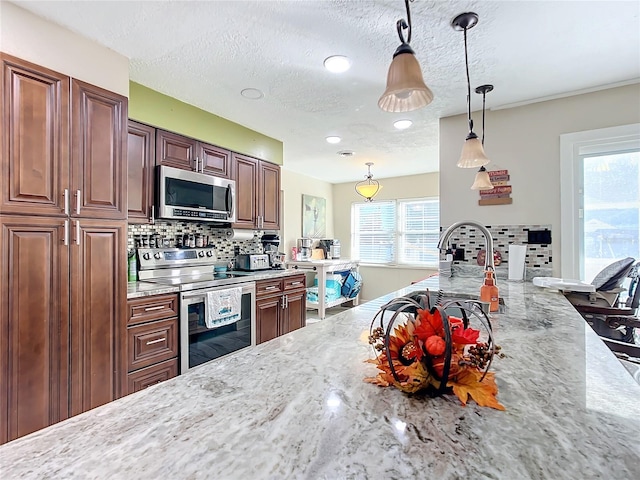 kitchen with hanging light fixtures, stainless steel appliances, tasteful backsplash, light stone counters, and a textured ceiling