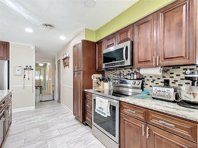 kitchen with a textured ceiling, backsplash, stainless steel appliances, and light stone counters