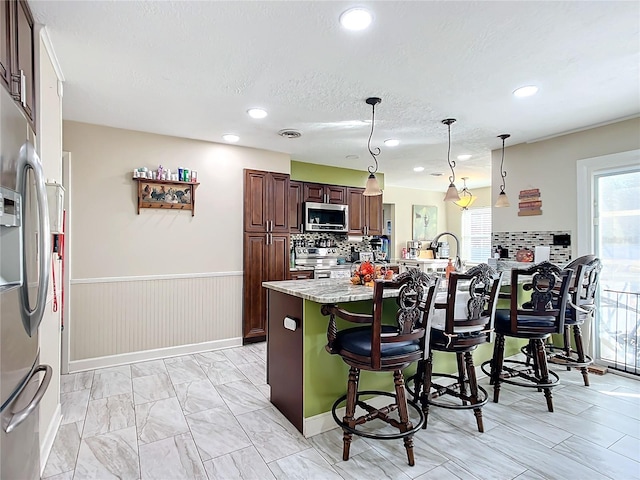 kitchen featuring light stone countertops, stainless steel appliances, an island with sink, decorative light fixtures, and a breakfast bar