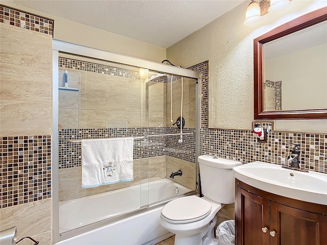 full bathroom featuring a textured ceiling, toilet, shower / bath combination with glass door, vanity, and tile walls