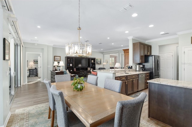 dining area with crown molding, light hardwood / wood-style flooring, a notable chandelier, and sink