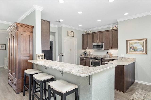 kitchen with kitchen peninsula, a breakfast bar, light hardwood / wood-style flooring, and stainless steel appliances