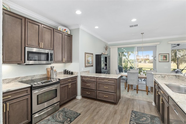 kitchen with appliances with stainless steel finishes, ornamental molding, dark brown cabinets, light hardwood / wood-style floors, and hanging light fixtures