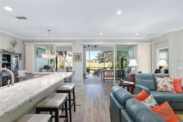 living room with light hardwood / wood-style flooring, a wealth of natural light, ornamental molding, and a notable chandelier