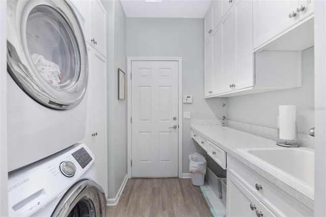 clothes washing area featuring light hardwood / wood-style floors, cabinets, sink, and stacked washer and clothes dryer