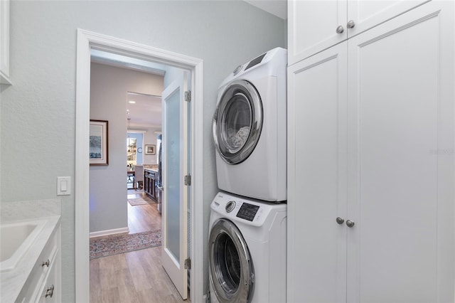 washroom with stacked washer / dryer, light hardwood / wood-style flooring, cabinets, and sink