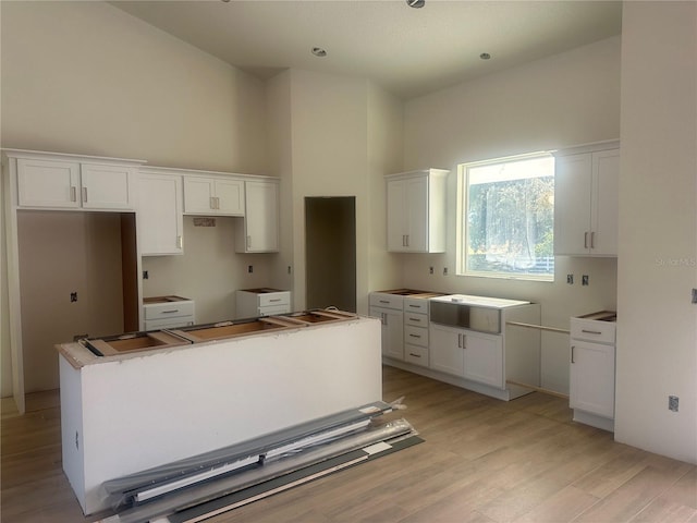 kitchen featuring white cabinets, a kitchen island, a towering ceiling, and light hardwood / wood-style flooring