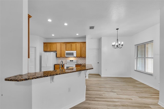 kitchen with a breakfast bar, white appliances, decorative light fixtures, light hardwood / wood-style flooring, and dark stone countertops