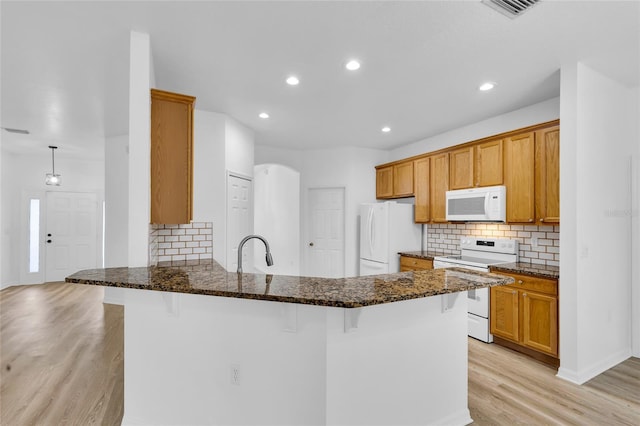 kitchen featuring a breakfast bar, dark stone countertops, white appliances, and kitchen peninsula