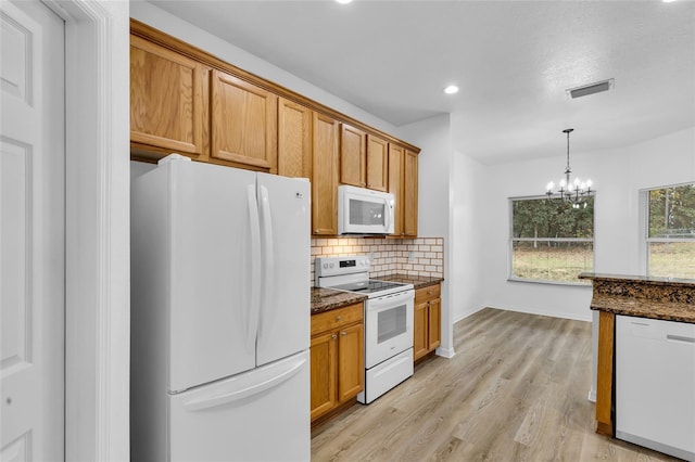 kitchen featuring white appliances, light hardwood / wood-style flooring, dark stone counters, and an inviting chandelier