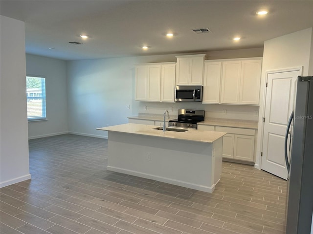 kitchen with white cabinets, stainless steel appliances, a kitchen island with sink, and light hardwood / wood-style floors