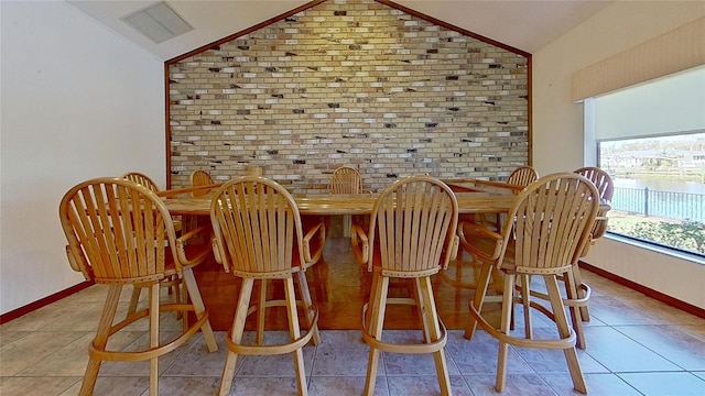 tiled dining area with bar, lofted ceiling, and brick wall