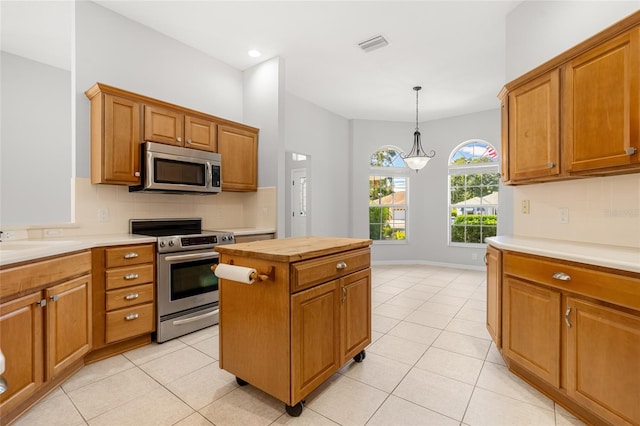 kitchen with appliances with stainless steel finishes, light tile patterned floors, a kitchen island, and pendant lighting