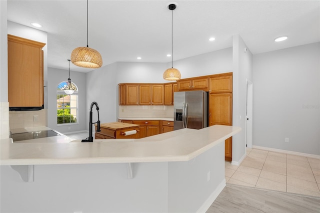 kitchen featuring kitchen peninsula, stainless steel refrigerator with ice dispenser, backsplash, pendant lighting, and a breakfast bar area