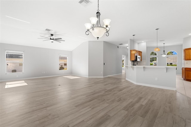 unfurnished living room with ceiling fan with notable chandelier, light hardwood / wood-style floors, vaulted ceiling, and a healthy amount of sunlight