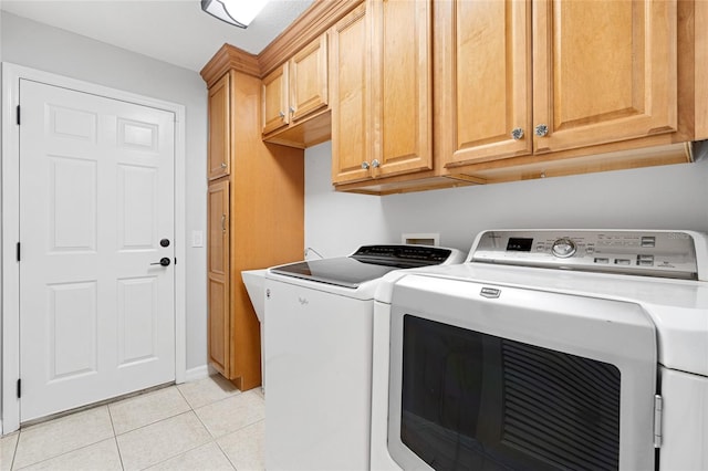 clothes washing area featuring washing machine and dryer, light tile patterned floors, and cabinets