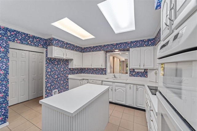 kitchen with light tile patterned flooring, white appliances, white cabinetry, and sink