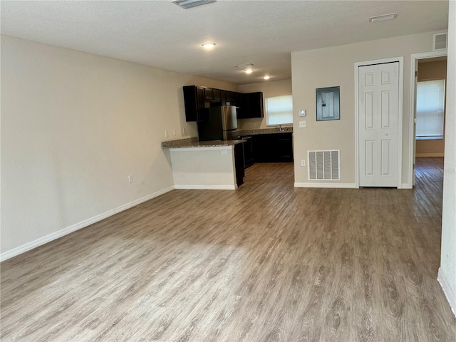 unfurnished living room featuring hardwood / wood-style floors, a textured ceiling, electric panel, and a healthy amount of sunlight