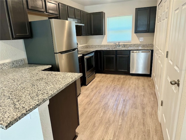 kitchen featuring light stone counters, kitchen peninsula, appliances with stainless steel finishes, and light hardwood / wood-style flooring