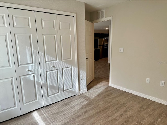 unfurnished bedroom featuring stainless steel fridge, light hardwood / wood-style flooring, and a closet