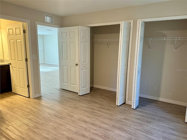 unfurnished bedroom featuring light wood-type flooring and multiple closets