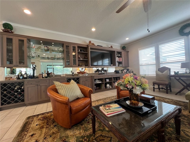 living room featuring ornamental molding, a textured ceiling, ceiling fan, indoor bar, and light tile patterned flooring