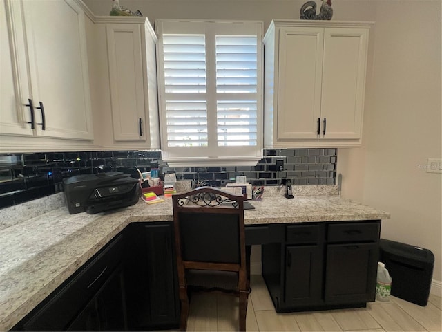 kitchen with light stone countertops, light tile patterned floors, tasteful backsplash, white cabinets, and built in desk