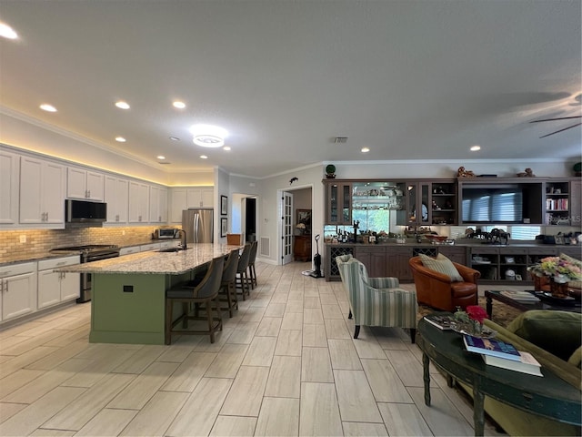 kitchen featuring a breakfast bar, white cabinets, a center island with sink, appliances with stainless steel finishes, and light stone counters