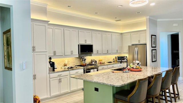 kitchen with light stone countertops, a kitchen island with sink, decorative backsplash, a breakfast bar, and appliances with stainless steel finishes