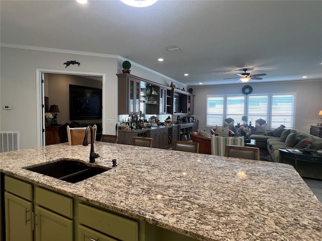 kitchen with light stone countertops, ornamental molding, ceiling fan, sink, and green cabinets