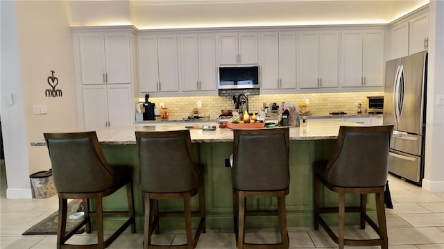 kitchen with appliances with stainless steel finishes, backsplash, light stone counters, a center island with sink, and white cabinets